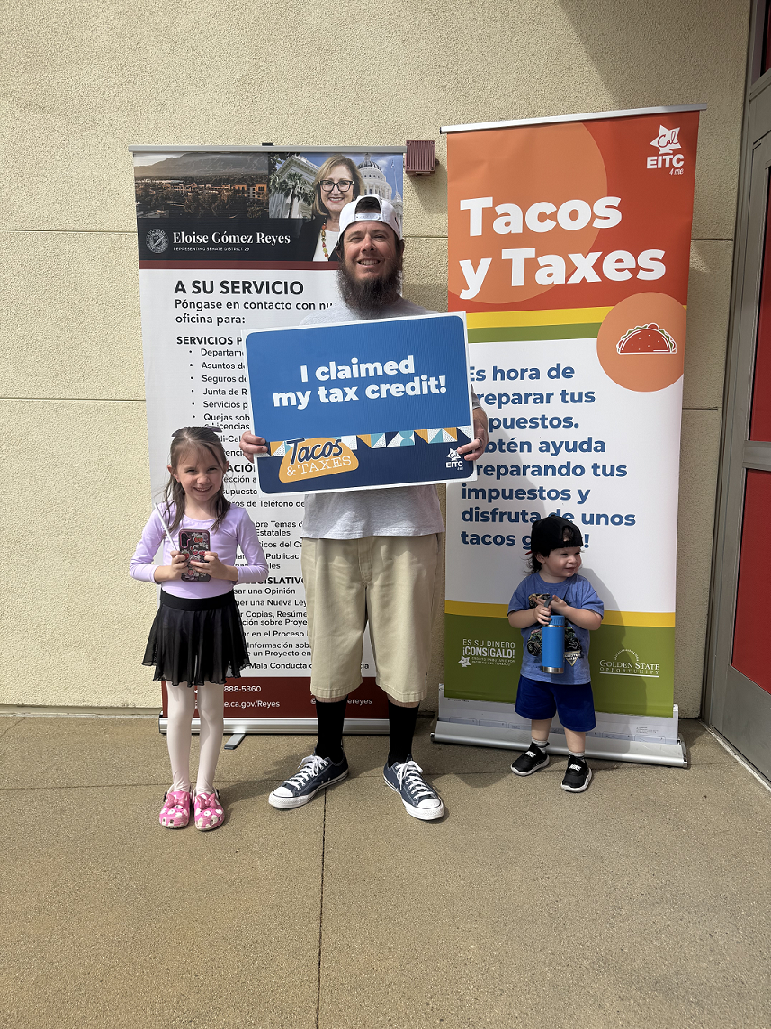 A man and two children pose with event signage